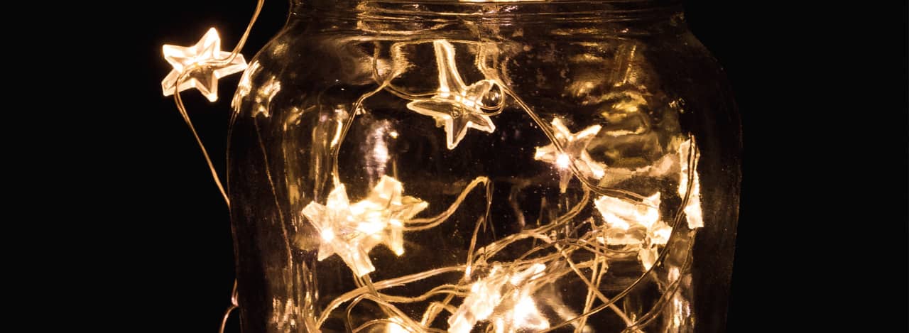 A photo of a mason jar against a dark background with a star string light inside of it